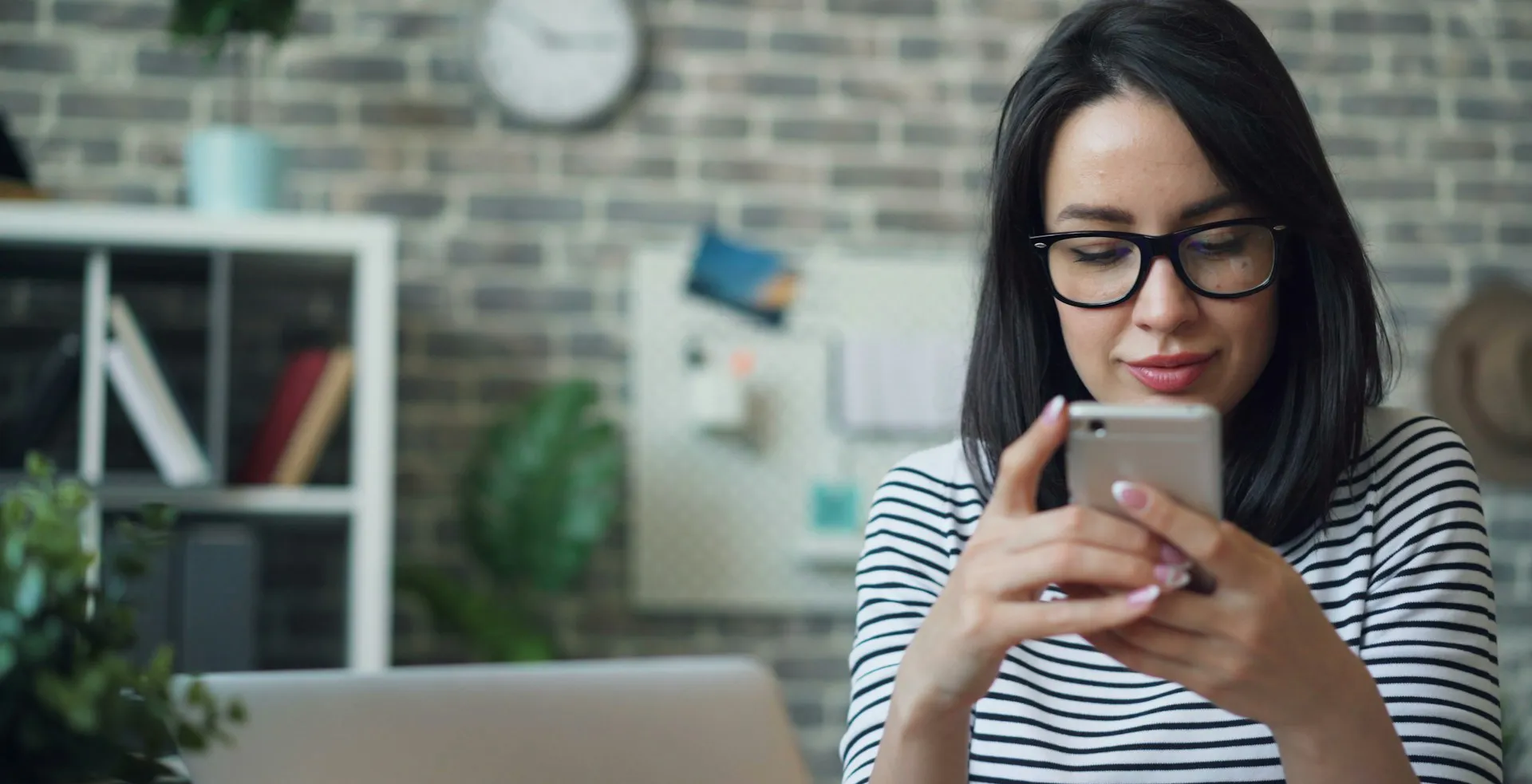 Una persona legge un messaggio sullo smartphone alla scrivania, con il portatile aperto davanti