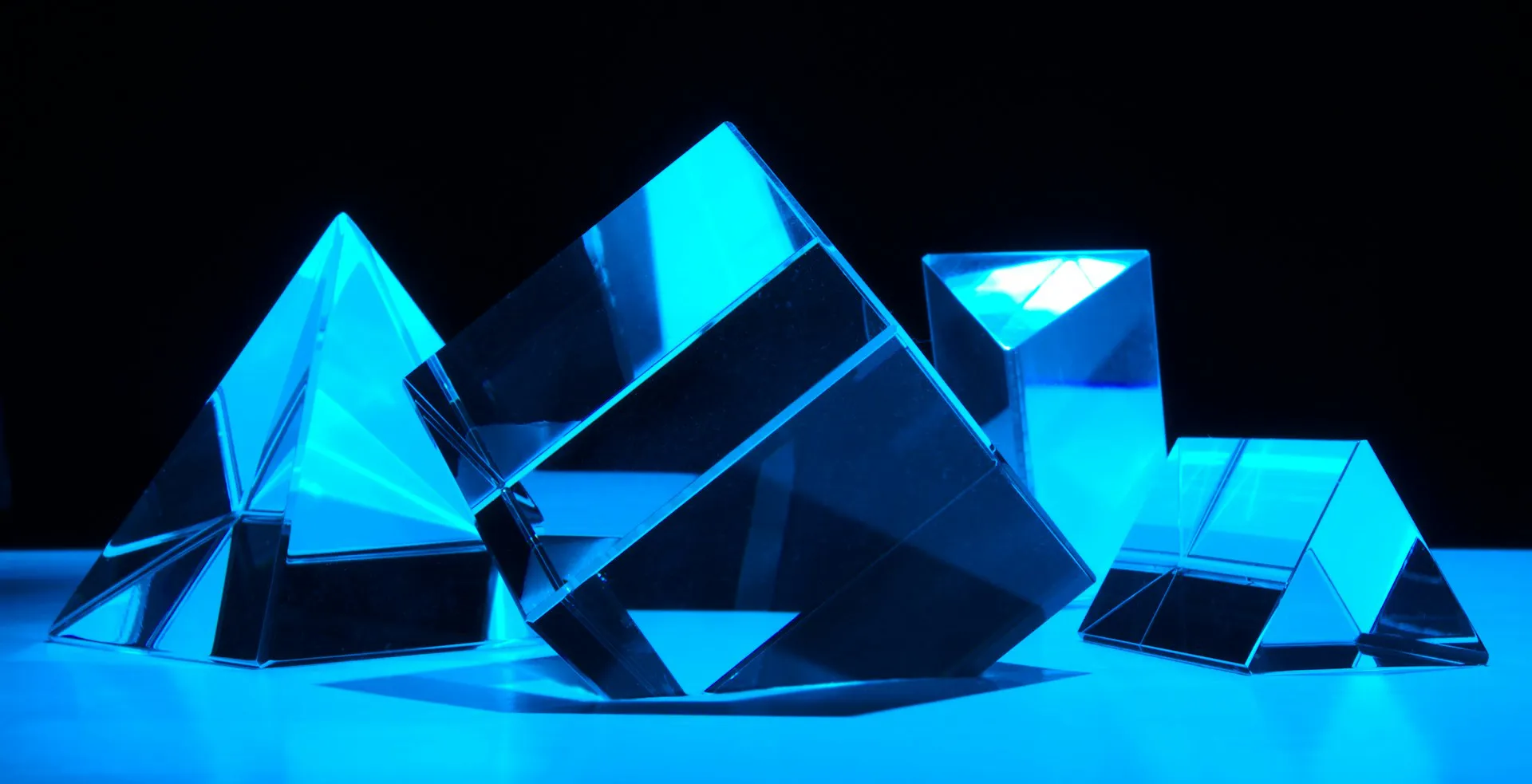 Diverse forme di cristallo, piramide, cubo e prisma, illuminate dalla stessa luce blu su sfondo scuro