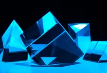 Diverse forme di cristallo, piramide, cubo e prisma, illuminate dalla stessa luce blu su sfondo scuro
