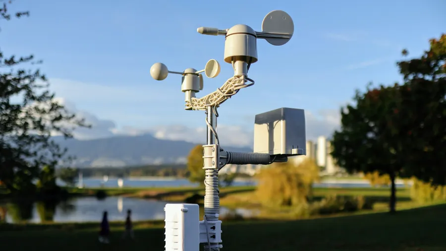 Stazione meteorologica bianca e beige su un'asta in un parco, con anemometro a coppe e sensori, sotto un cielo azzurro: gli strumenti per misurare il rischio climatico